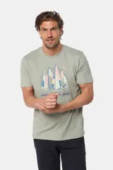 Remera de manga corta color verde grisáceo con cuello redondo. Presenta un estampado frontal de veleros sobre un fondo circular con líneas verticales, y texto bordado debajo.