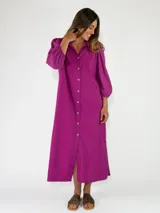 Vestido midi de algodón color fucsia, con cuello camisero, cierre frontal con botones y mangas largas abullonadas con detalles bordados.