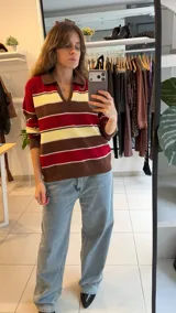 Sweater tejido de punto con diseño a rayas horizontales en tonos amarillo, celeste y marrón. Presenta un cuello polo con escote en V, mangas largas y un corte holgado.