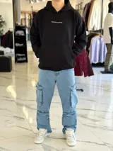 Canguro oversize negro con capucha y bolsillo tipo canguro. Presenta un gran estampado en la espalda con la inscripción "Own Your Story", texto descriptivo y un gráfico de globo terráqueo junto al año "2021".