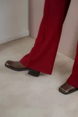 Botas tipo chelsea de cuero color marrón oscuro con acabado brillante. Presentan punta cuadrada con detalle de puntera metálica, elásticos laterales y taco cuadrado bajo.