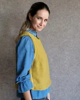 Chaleco de tela bucle color tostado, con diseño sin mangas, cuello redondo y corte recto. Presenta costuras verticales decorativas en el frente.