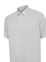 Camisa de manga corta confeccionada en lino orgánico, con cuello clásico y cierre frontal de botones. Presenta un diseño minimalista con un pequeño logo bordado en el pecho.