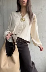 Camisa beige de manga larga con diseño abullonado y puños elastizados, escote en V con botones frontales y sutiles bordados florales tono sobre tono.