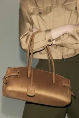 Cartera de hombro color tostado, con doble asa superior y detalle de tiras laterales ajustables. Cuenta con cierre magnético y etiqueta colgante.