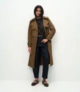 Trench coat largo de Marfinno, confeccionado en gabardina de poliéster. Presenta cuello con solapas, aletas en los hombros, cierre frontal con botones y cinta para lazo en la cintura.