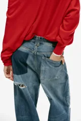 Jeans de tiro medio y corte baggy con cinco bolsillos, trabillas y rotos decorativos. Cuenta con detalle de cinturón confeccionado en el mismo tejido y cierre frontal con cremallera y botón metálico.