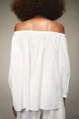 Blusa blanca de lino con escote recto y hombros descubiertos, manga abullonada tres cuartos terminada en elástico.