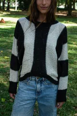Sweater de punto con diseño de rayas verticales anchas en colores negro y crema. Presenta un tejido con sutiles lentejuelas incorporadas que aportan brillo a la prenda, cuello redondo y mangas largas con puños ajustados.