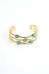Brazalete rígido de metal dorado con diseño de tres tiras onduladas y aplicación de piedras turquesas ovaladas.