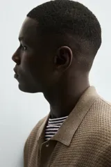 Camisa de punto de manga corta, color marrón topo, con cuello solapa y cierre frontal de botones. Presenta un tejido texturizado y un calce relajado.