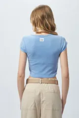 Top corto de manga corta, color negro con efecto desgastado o acid wash, cuello redondo y costuras verticales que definen la silueta.