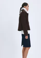 Chaqueta de algodón estilo tejano de corte recto, color marrón, con cuello camisero de efecto piel en contraste, manga larga y dos bolsillos de parche con solapa y botón en el frente. Cuenta con cierre oculto de cremallera y botones.
