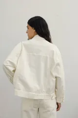 Campera de jean color crudo, con cuello camisero, cierre frontal con botones y bolsillos con solapa en el pecho.