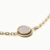 Pulsera dorada de cadena fina con dije circular de nácar.