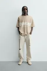 Sudadera de corte relajado, color beige claro, con cuello redondo y manga corta. Presenta un estampado frontal con texto en blanco difuminado que dice "SCREEN PLAYER" y debajo "Hypercore Technology".