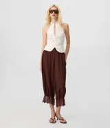 Pantalón bloomer marrón de cintura alta, confeccionado en viscosa con textura crinkle. Cuenta con un diseño amplio y cómodo, perneras voluminosas, puños con elástico interno y aplicación de encaje floral en los puños.