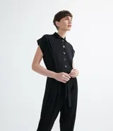 Mono largo de malla jersey color negro, con cuello tipo camisa, cierre frontal abotonado, sin mangas y cinturón de la misma tela para ajustar en la cintura.
