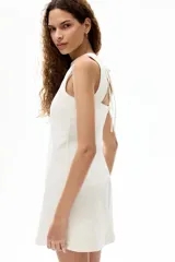 Vestido corto sin mangas de sarga de algodón en color blanco, con leve corte evasé, escote redondo y tiras finas para atar en la nuca.
