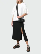 Cartera tipo crossbody de diseño rectangular, color negro, con cierre superior y logo metálico frontal. Incluye correa ajustable con diseño de marca.