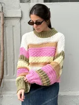 Buzo de tejido de punto grueso con diseño de rayas horizontales multicolores en tonos blanco, rosa, verde oliva y beige. Presenta cuello redondo acanalado, mangas largas con puños ajustados y un corte holgado.