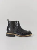 Bota corta de cuero negro con textura tipo cocodrilo, diseño de punta cuadrada y costuras decorativas en color contrastante. Cuenta con suela plana de dos tonos y tirador en la parte trasera.