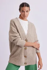 Cardigan de punto en color beige, con escote en V, cierre frontal con botones de carey y mangas largas con puños acanalados. Presenta un diseño holgado y tejido con textura.