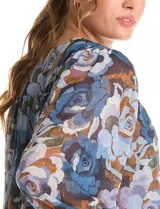 Blusa de gasa con estampado floral en tonos azules y marrones, con sutiles hilos de lurex dorados. Presenta cuello a la base, abertura central con botones, canesú delantero con pasamanería calada y mangas largas con puños elastizados. Incluye forro interno a tono.