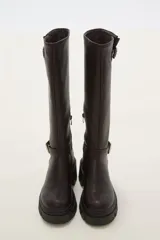 Bota de caña alta color negro, confeccionada en eco cuero, con suela track de goma y detalle de hebilla metálica en el tobillo y en la parte superior de la caña.