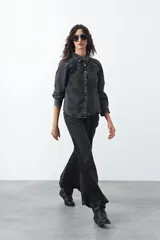 Camisa de jean color azul claro con tachas metálicas en el canesú y a lo largo de las costuras frontales. Tiene mangas largas con puños abullonados y cierre frontal con botones.