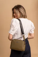 Bandolera de diseño compacto con textura granulada, color verde oliva. Cuenta con una correa ajustable de tela negra con el logo de la marca en relieve y placa metálica frontal con el nombre de la marca.
