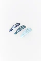 Pack de tres clips para el cabello tipo broche, en tonos de azul. Uno es azul oscuro con estampado floral blanco, otro es azul grisáceo con textura tramada y el tercero es celeste liso.