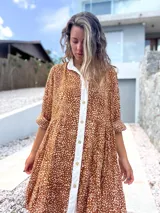 Vestido camisero de corte holgado y diseño escalonado, con estampado de pequeñas manchas blancas sobre fondo terracota. Presenta cuello camisero, cierre frontal con botones y mangas largas con puños.