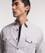 Camisa de manga larga Marfinno en tejido de sarga color gris, con cuello camisero, cierre frontal de botones y dos bolsillos frontales con solapa y botón.