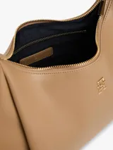 Cartera tipo hobo de Tommy Hilfiger en color beige, con acabado liso, cierre de cremallera, asa superior y correa ajustable y extraíble. Cuenta con el logo metálico de la marca en relieve en la parte delantera.