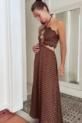 Vestido largo de satén color marrón con estampado de lunares blancos. Presenta un diseño cut-out en la cintura, escote halter con detalle de mostacillas y terminaciones con puntilla negra en el top.