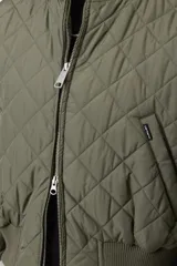 Campera matelaseada de color verde militar, con diseño acolchado en forma de rombos, cuello, puños y dobladillo en punto acanalado, cierre frontal completo y corte estilo bomber.