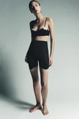 Shorts de tiro alto, color negro, confeccionado en tejido semitransparente de poliamida. La cintura es elástica y el bajo está rematado con una aplicación de encaje en tono beige/dorado.