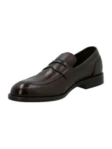 Mocasín estilo penny loafer para hombre, confeccionado en cuero marrón oscuro con textura sutil, punta redonda y suela plana con pequeño tacón.