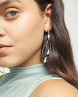 Pendientes colgantes con base de bola plateada, tiras de cuero negro formando un doble lazo y detalles de bolas plateadas en el interior y en la parte inferior.