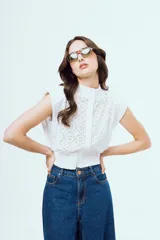 Top blanco sin mangas de broderie, con cuello alto, hombreras y cierre frontal de botones.
