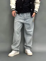 Pantalón de jean estilo baggy de corte ancho y relajado, color azul claro con lavado desgastado. Presenta un bordado en el bolsillo trasero derecho con un diseño de llamas y las siglas SDA.