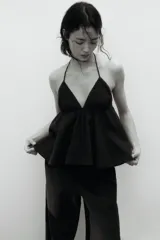 Top halter de algodon negro en muselina con escote en V y tiras que se anudan en el cuello. Presenta un diseño con costura fruncida debajo del busto y silueta acampanada.