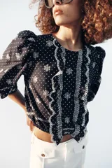 Blusa azul marino con estampado de lunares blancos, cuello redondo y mangas abullonadas. Presenta detalles de bordados perforados, volantes delanteros y acabados elásticos.