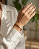 Pulsera tipo esclava rígida de acero con baño de oro, con diseño grabado en su superficie.