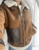 Chaqueta marrón con cuello de piel sintética color crema, cierre frontal con cremallera y hebilla en el cuello, bolsillos laterales con ribete de cuero marrón y puños con ribete de piel sintética.