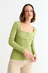 Remera de manga larga, color blanco, con tejido acanalado y escote cuadrado. Presenta un cierre metálico dorado en el centro del escote.