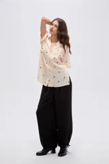 Camisa de lyocell color beige con estampado de lunares negros, cuello solapa, manga corta y cierre frontal con botones.
