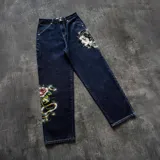 Pantalón de jean color azul oscuro con corte baggy, presenta estampados gráficos estilo tatuaje en ambas piernas.