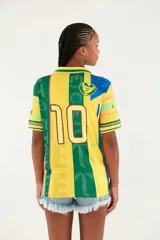 Camiseta deportiva estilo polo, de manga corta, con diseño estampado multicolor en tonos amarillo y verde, inspirada en camisetas de fútbol.